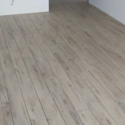 Ułożona pod kątem podłoga z płytek imitujących drewno w odcieniach szarości, z widocznymi fugami i fragmentem białej ściany w tle.