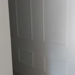 Białe ściany z dekoracyjnymi panelami w kształcie prostokątów, jasna podłoga imitująca drewno, minimalistyczne wnętrze.