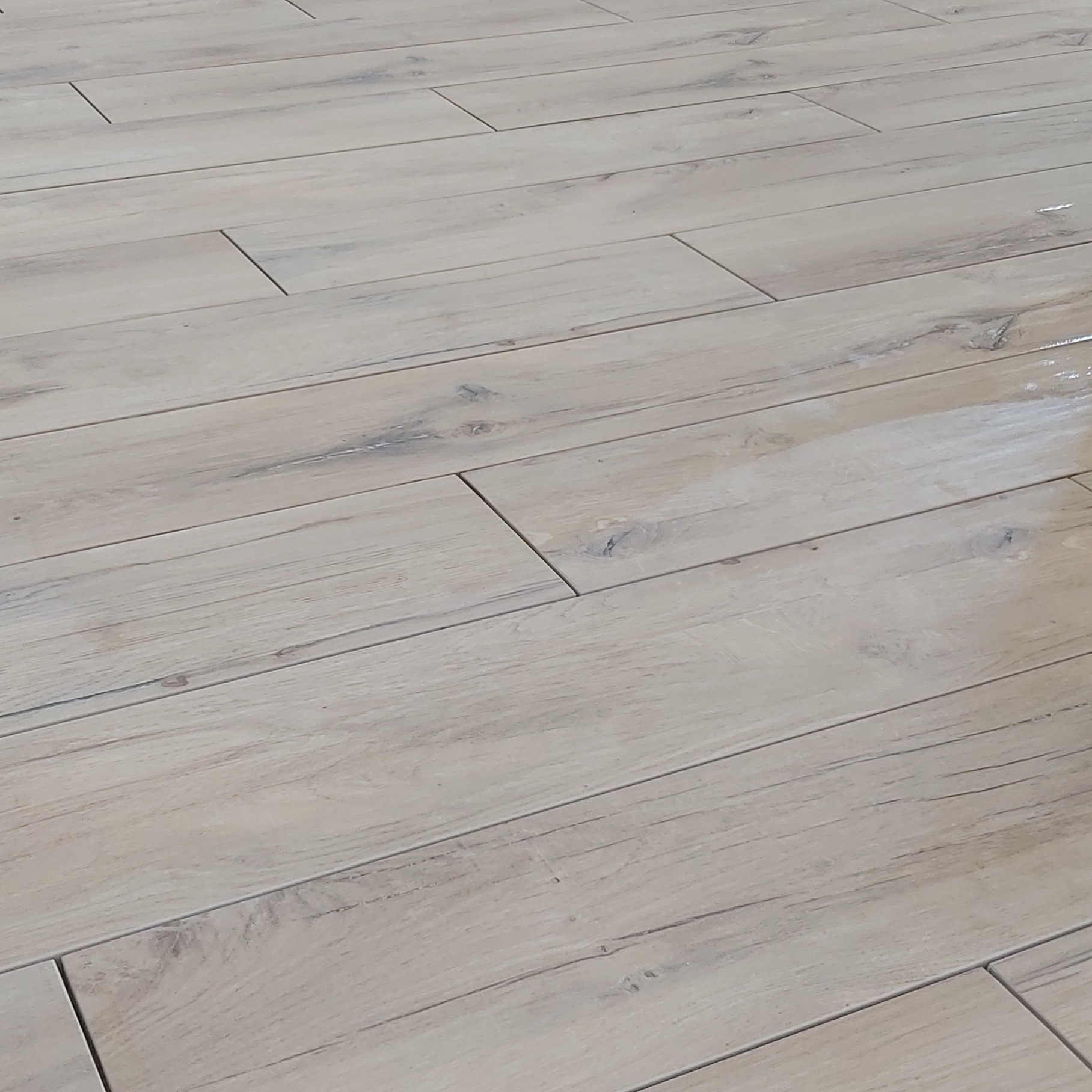 Jasne, podłużne płytki podłogowe imitujące drewno, ułożone równolegle do siebie, z widoczną strukturą i delikatnymi szarymi akcentami.