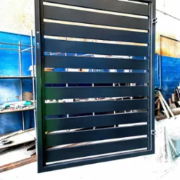 Ciemnoszara brama z poziomych profili, widoczna w warsztacie z niebieską ścianą i rusztowaniem w tle.