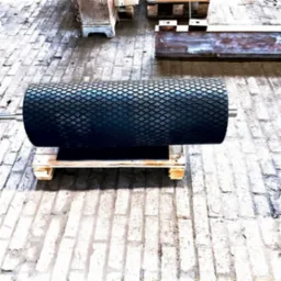 Czarny, gumowany walec z romboidalnym wzorem powierzchni, umieszczony na drewnianej palecie, widoczny na tle betonowej posadzki w hali produkcyjnej.