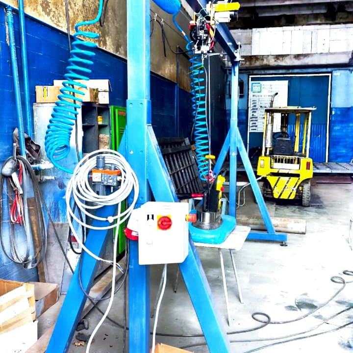 Niebieski, stalowy system podnoszenia z elementami pneumatycznymi i elektrycznymi w warsztacie, z widocznym w tle wózkiem widłowym.