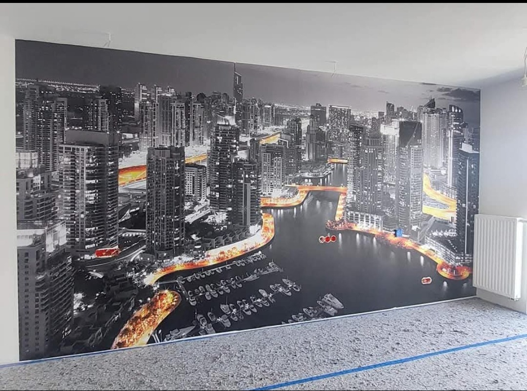 Fototapeta z motywem panoramy miasta na ścianie w pokoju, widoczny grzejnik i przygotowane podłoże pod panele.