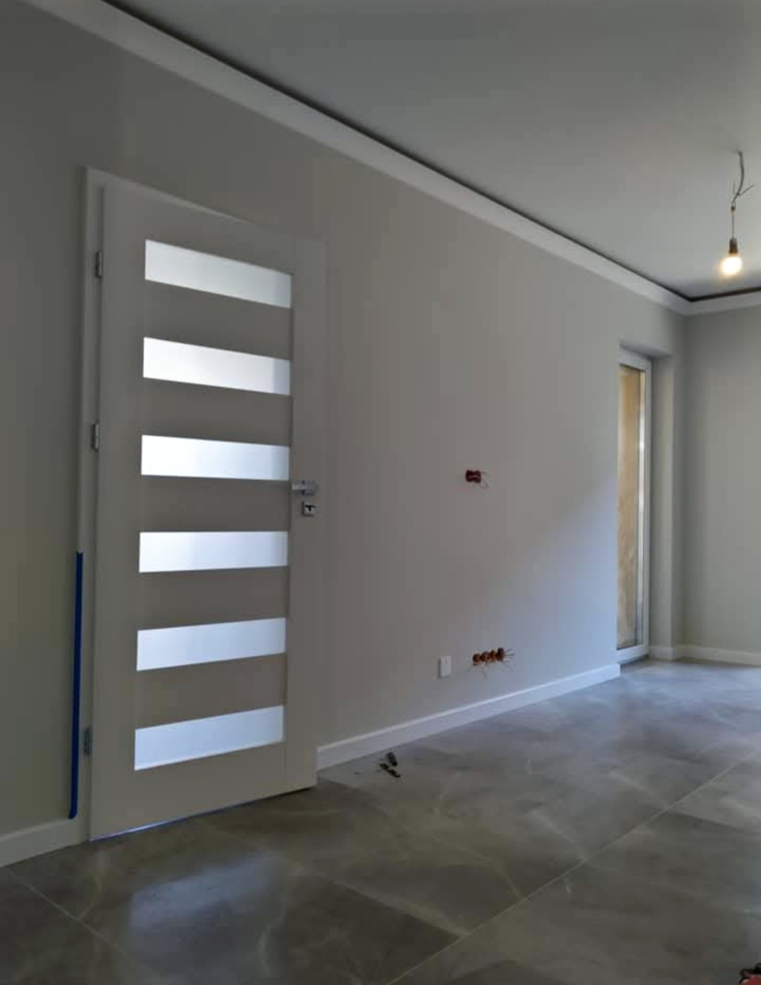 Nowoczesne wykończenie wnętrza: szare ściany, białe listwy przypodłogowe, drzwi z przeszkleniami i marmurowe płytki podłogowe.