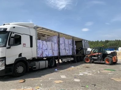 Załadunek sprasowanych bel papieru do niszczenia na naczepę ciężarówki za pomocą wózka widłowego Bobcat, teren składowiska.