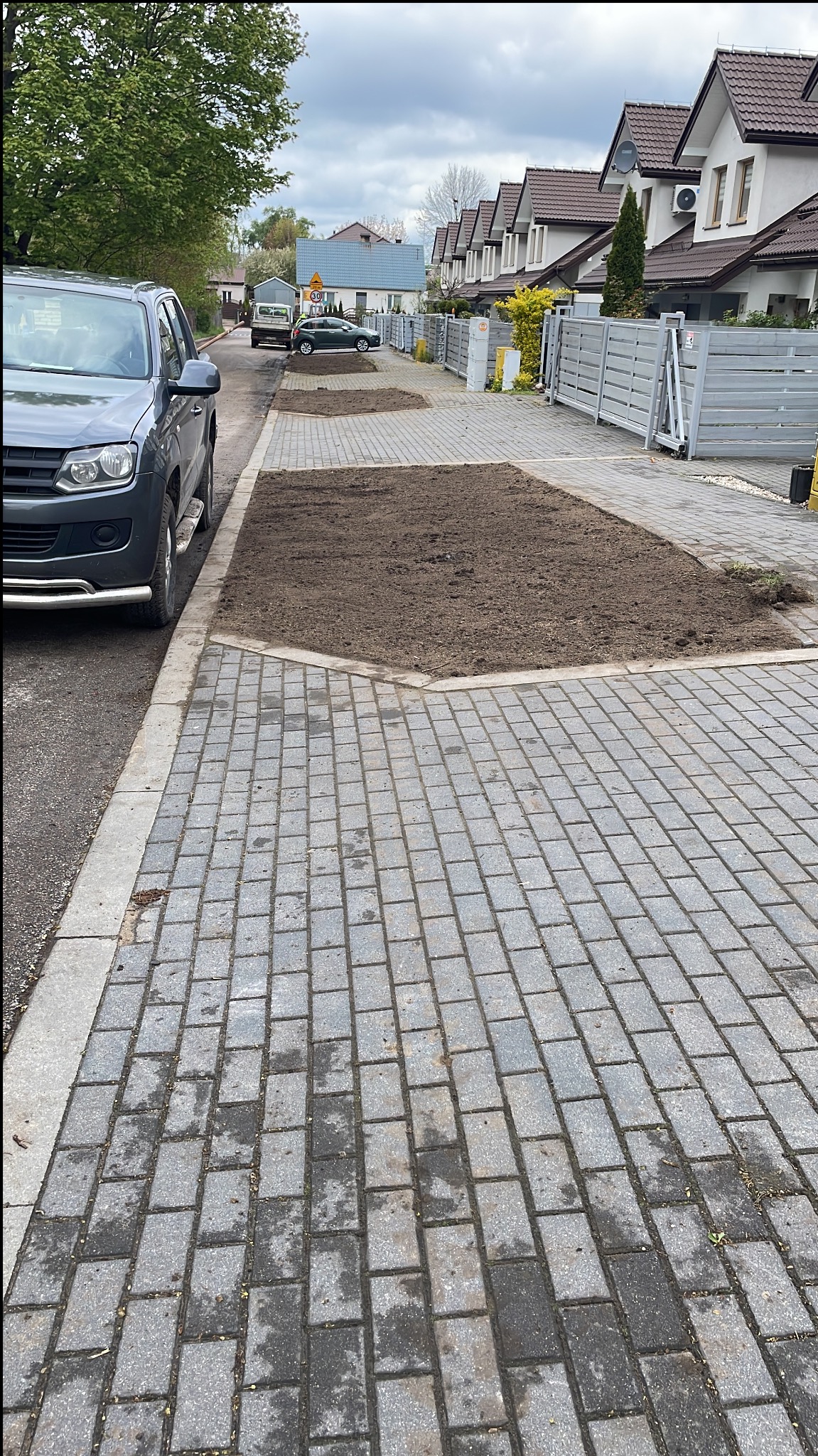 Przygotowane rabaty z ziemią pod trawnik z rolki, obramowane kostką brukową, na podjeździe przed domami jednorodzinnymi.