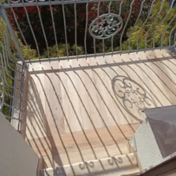 Balkon wyłożony płytkami imitującymi drewno, z metalową balustradą rzucającą cienie na podłogę.