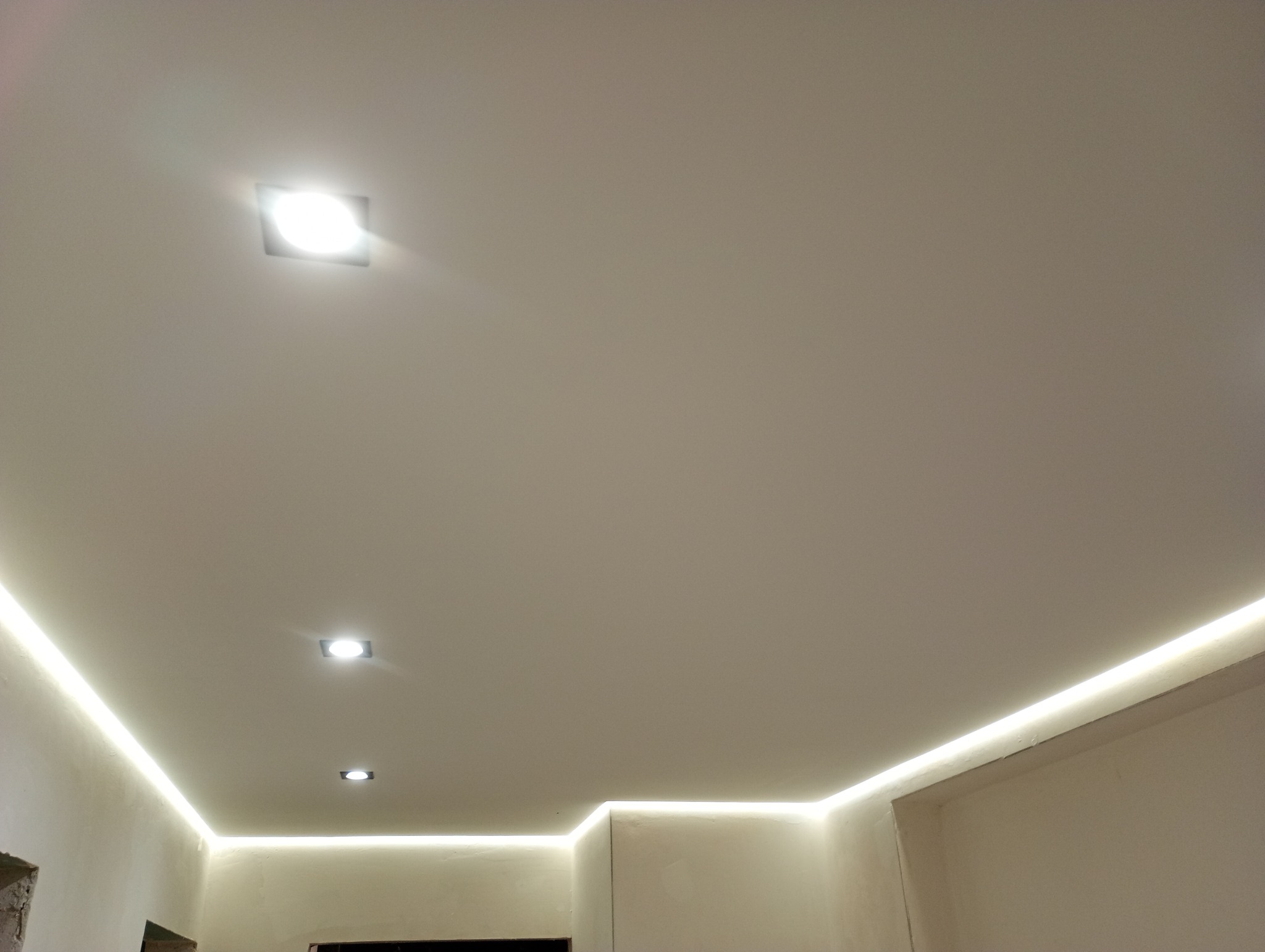 Podwieszany sufit z oświetleniem LED wzdłuż krawędzi i trzema punktowymi lampami kwadratowymi, widok z dołu.