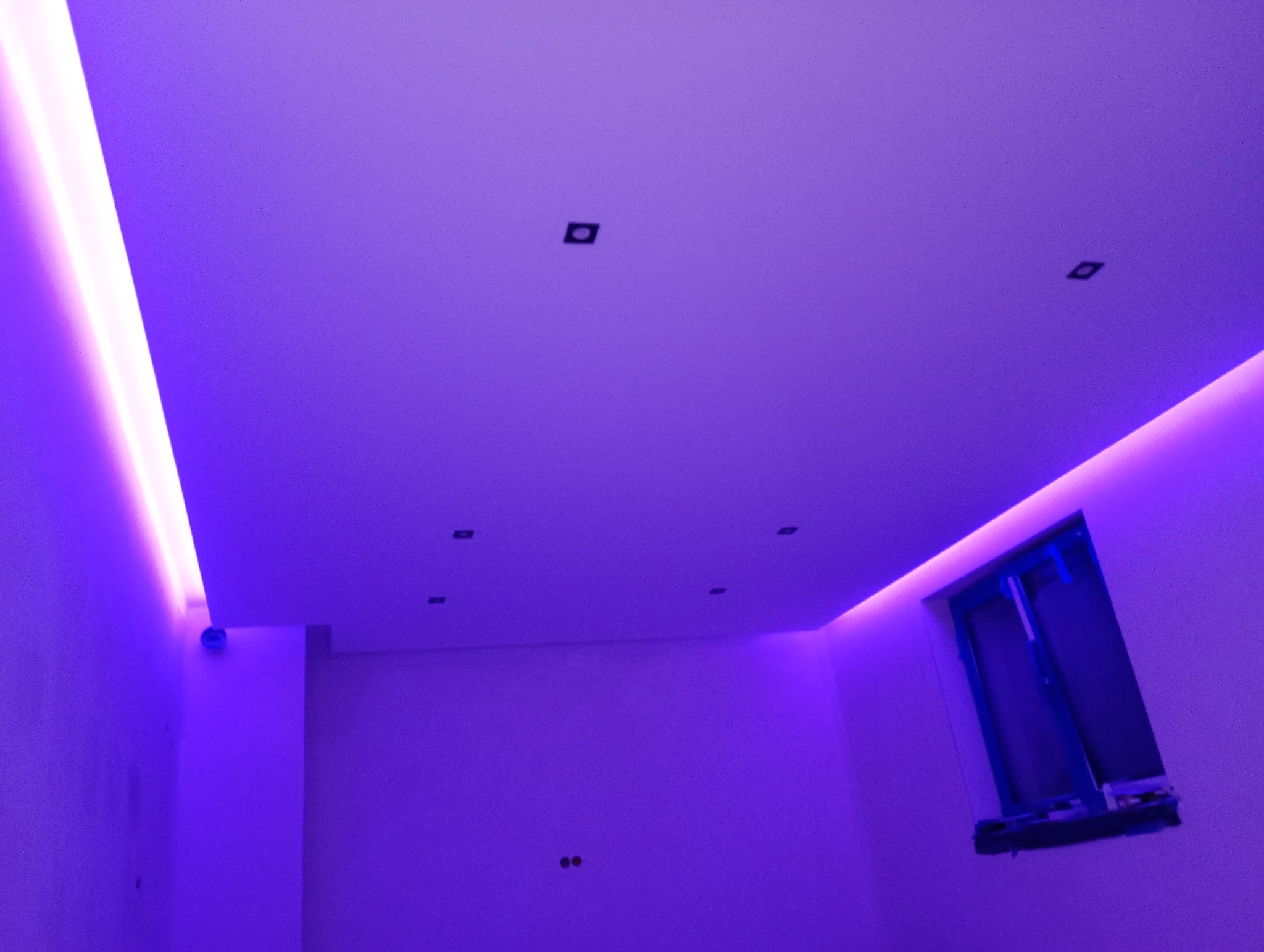 Wnętrze pokoju z oświetleniem LED w kolorze fioletowym, widoczne punkty świetlne na suficie i okno z zabezpieczeniem.
