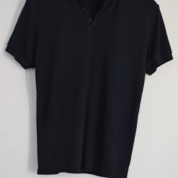 UNETI Leszek Janczalik - Granatowa koszulka polo marki ZARA, zawieszona na plastikowym wieszaku na tle białej ściany, widoczne trzy guziki i krótki rękaw.