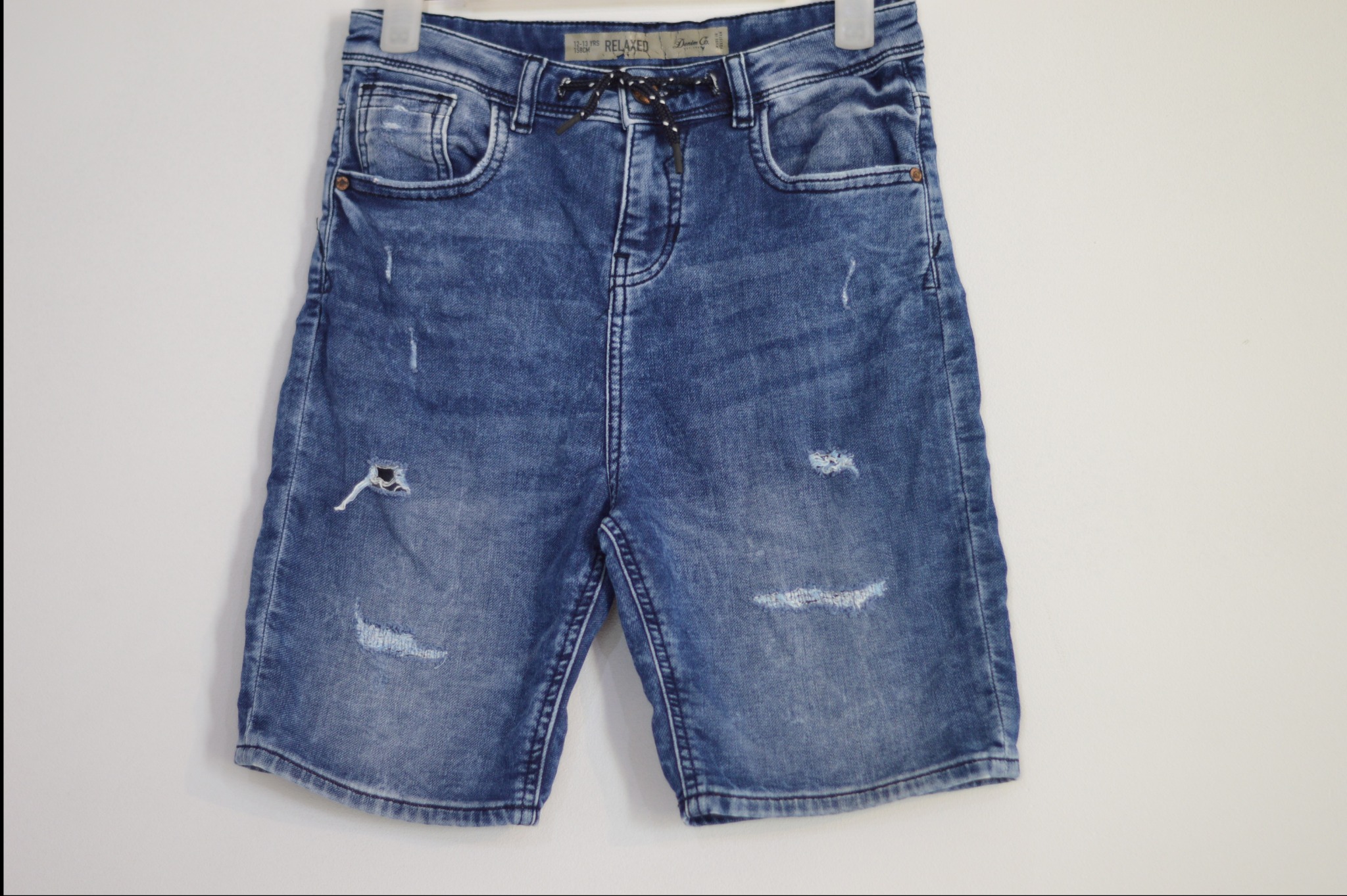 Dżinsowe spodenki męskie z efektem sprania i przetarciami, wiszące na wieszaku na białym tle.