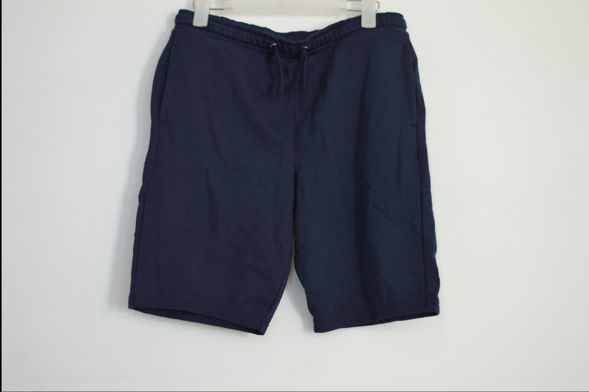 Granatowe, bawełniane spodenki dresowe męskie, wiszące na wieszaku na białym tle.