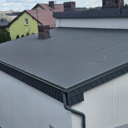 Dach wykonany z blachy trapezowej w kolorze grafitowo-szarym. Widoczne staranne obróbki blacharskie: pas nadrynnowy i narożniki w tym samym kolorze co pokrycie główne.