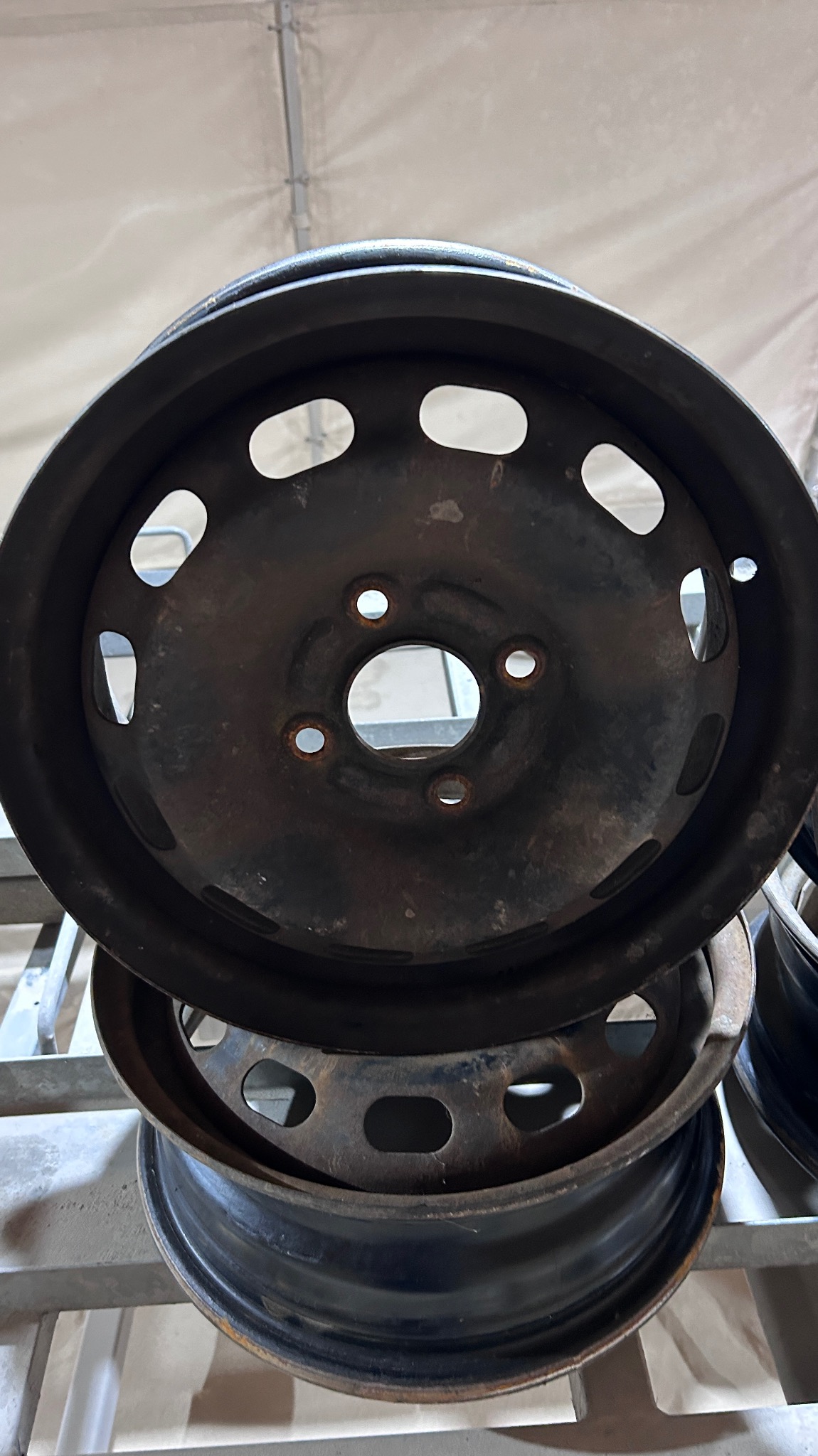 Stos starych, pordzewiałych felg stalowych z owalnymi otworami wentylacyjnymi, czekających na renowację.