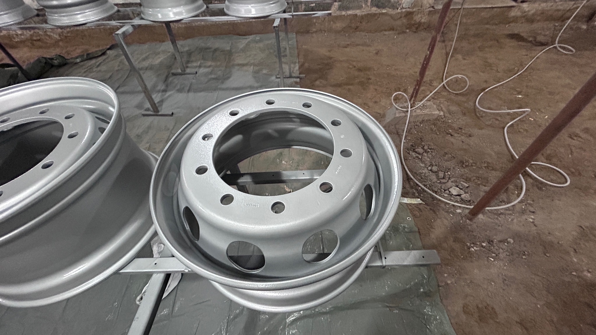 Dwa świeżo pomalowane na szaro felgi samochodowe na metalowych stojakach w warsztacie, widoczne napisy na jednej z felg.