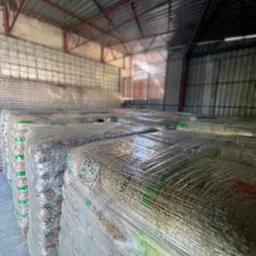 Skladowane, owinięte folią palety z pelletem drzewnym w magazynie z metalową konstrukcją dachu i ceglaną ścianą w tle. Na opakowaniach widoczne certyfikaty jakości.