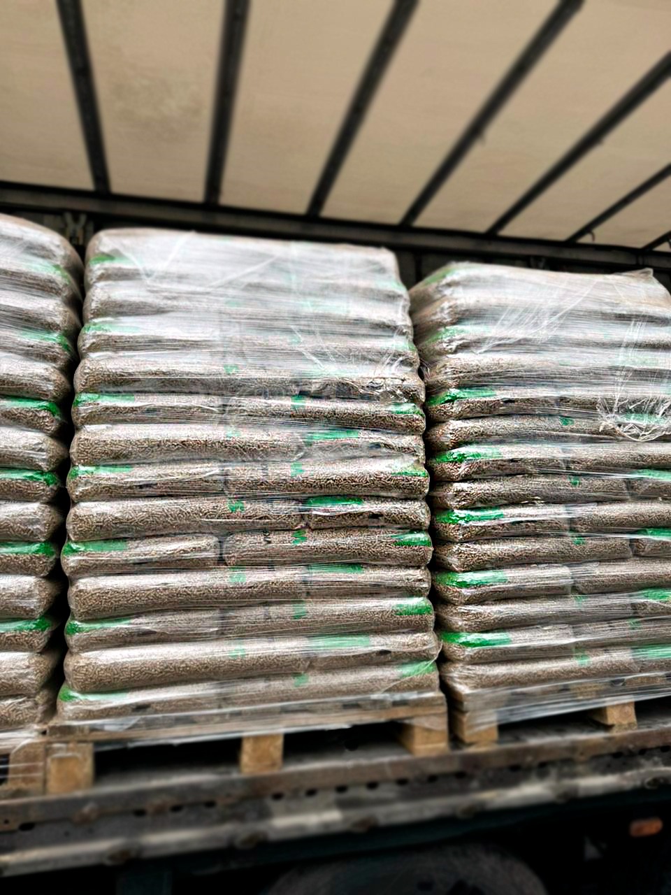 Palety z workami pelletu drzewnego, zabezpieczone folią, ułożone w rzędach wewnątrz pojazdu dostawczego.