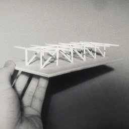 Archi Analysis - Czarno-białe zdjęcie dłoni trzymającej architektoniczną makietę konstrukcji budynku z białych elementów na płycie.