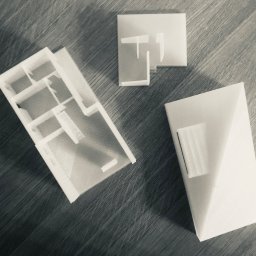 Archi Analysis - Makieta architektoniczna budynku: rzut parteru z widocznymi schodami, fragment dachu i element elewacji, wykonane z białego tworzywa, leżą na drewnianej powierzchni.