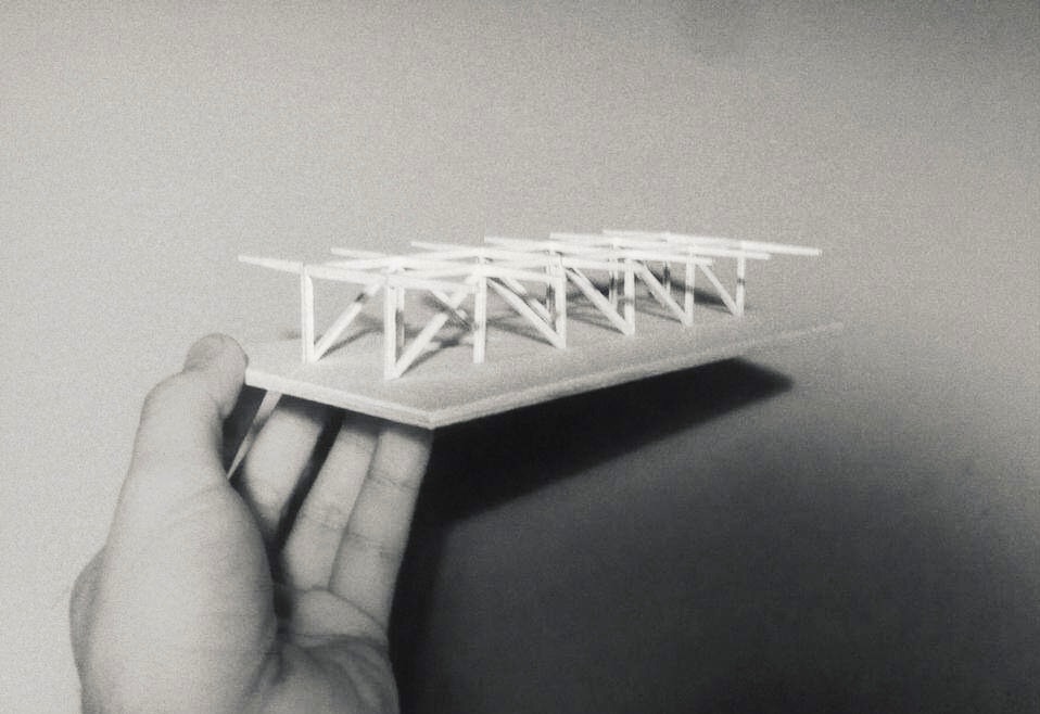 Czarno-białe zdjęcie dłoni trzymającej architektoniczną makietę konstrukcji budynku z białych elementów na płycie.