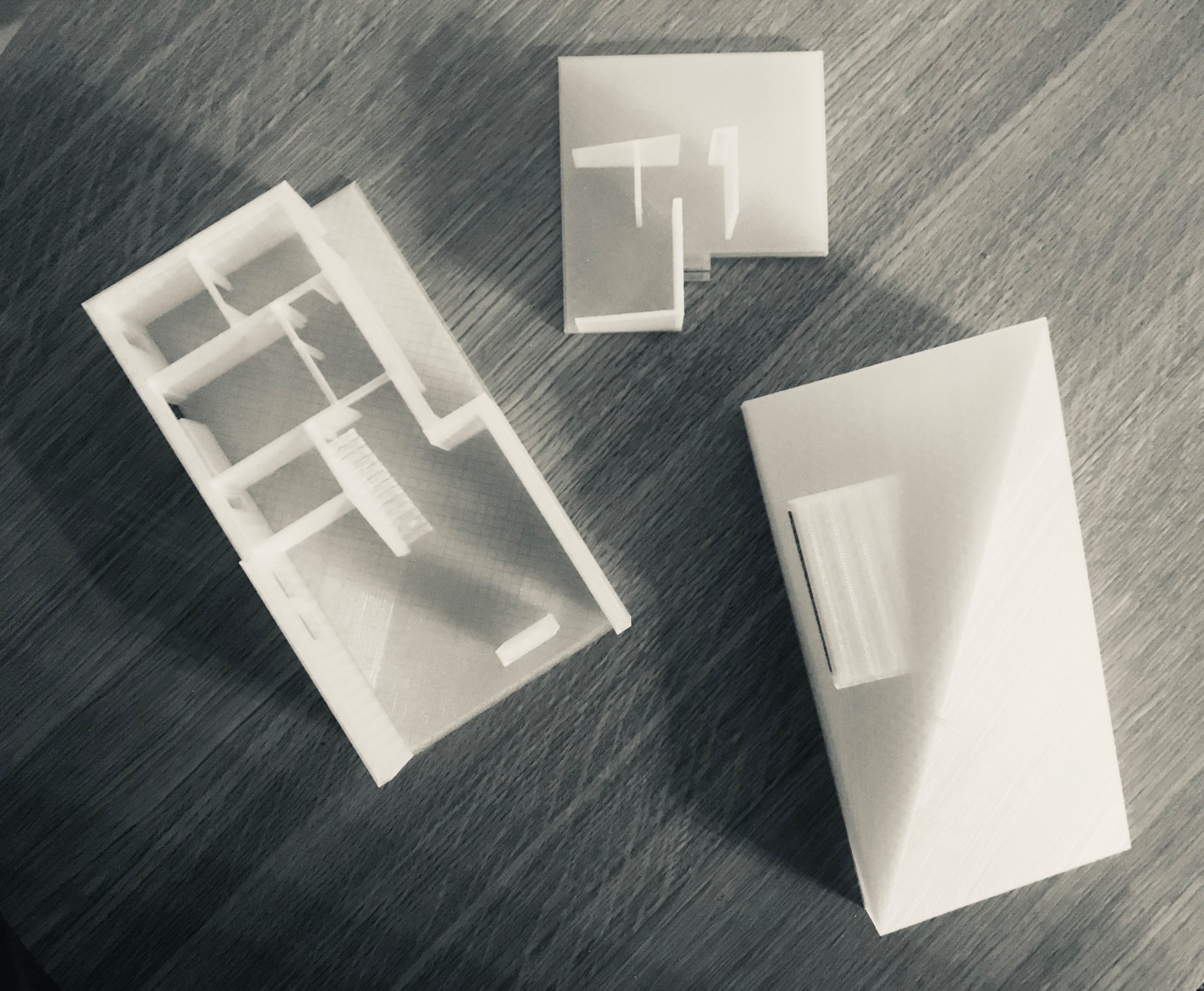 Makieta architektoniczna budynku: rzut parteru z widocznymi schodami, fragment dachu i element elewacji, wykonane z białego tworzywa, leżą na drewnianej powierzchni.