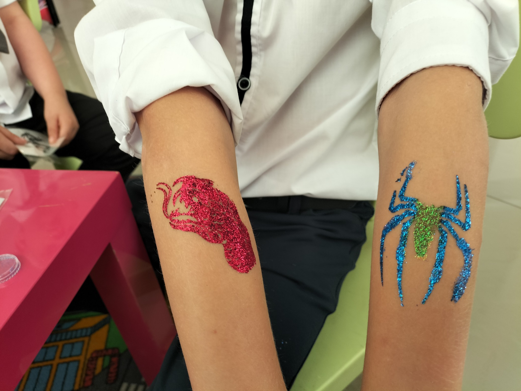 Brokatowe tatuaże na ramionach dziecka: czerwony smok i niebiesko-zielony pająk. Biała koszula z czarną lamówką. Kreatywna zabawa dla dzieci.