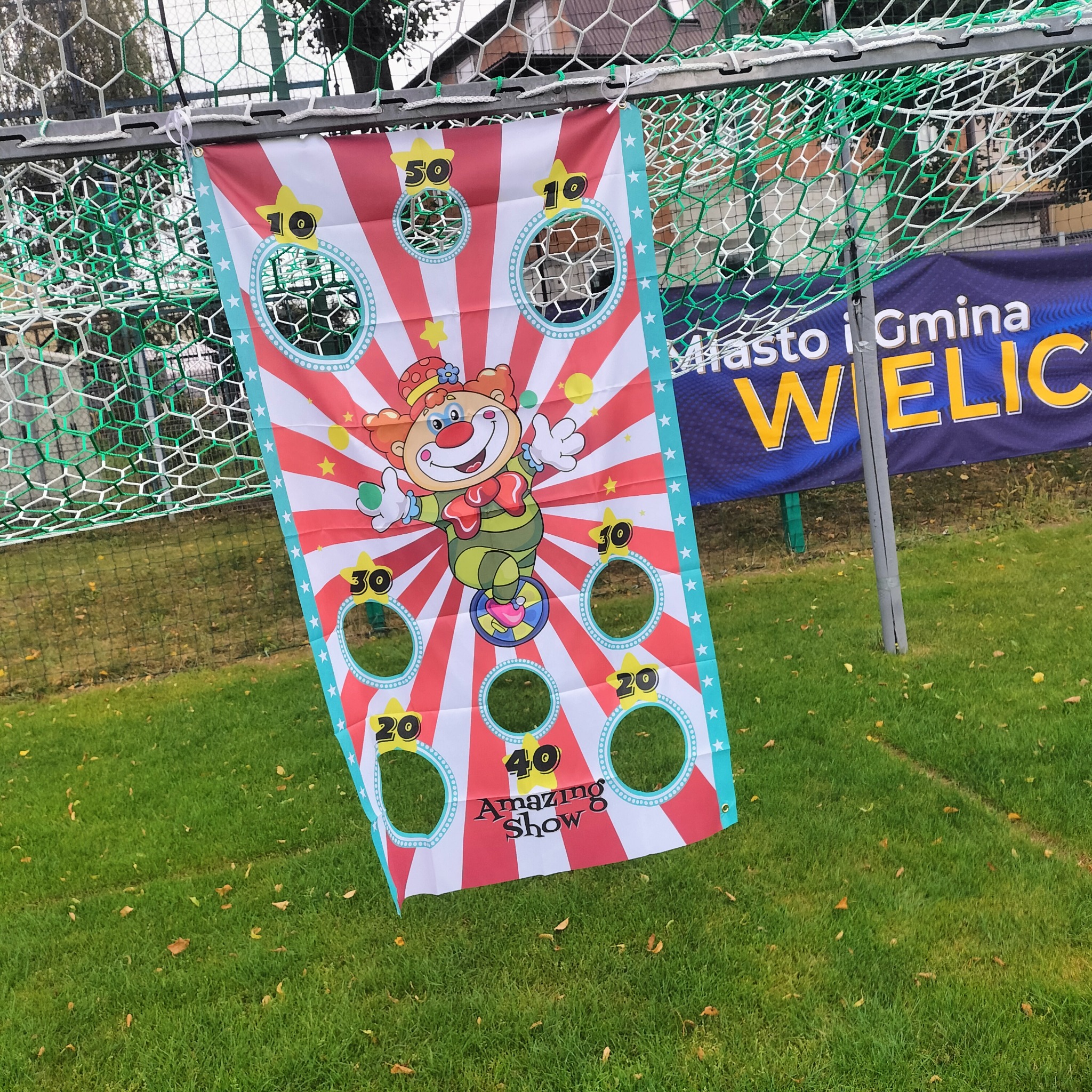 Atrakcja dla dzieci: kolorowa plansza z motywem klauna i otworami do rzucania, zawieszona na bramce piłkarskiej. Gra zręcznościowa na imprezę plenerową.