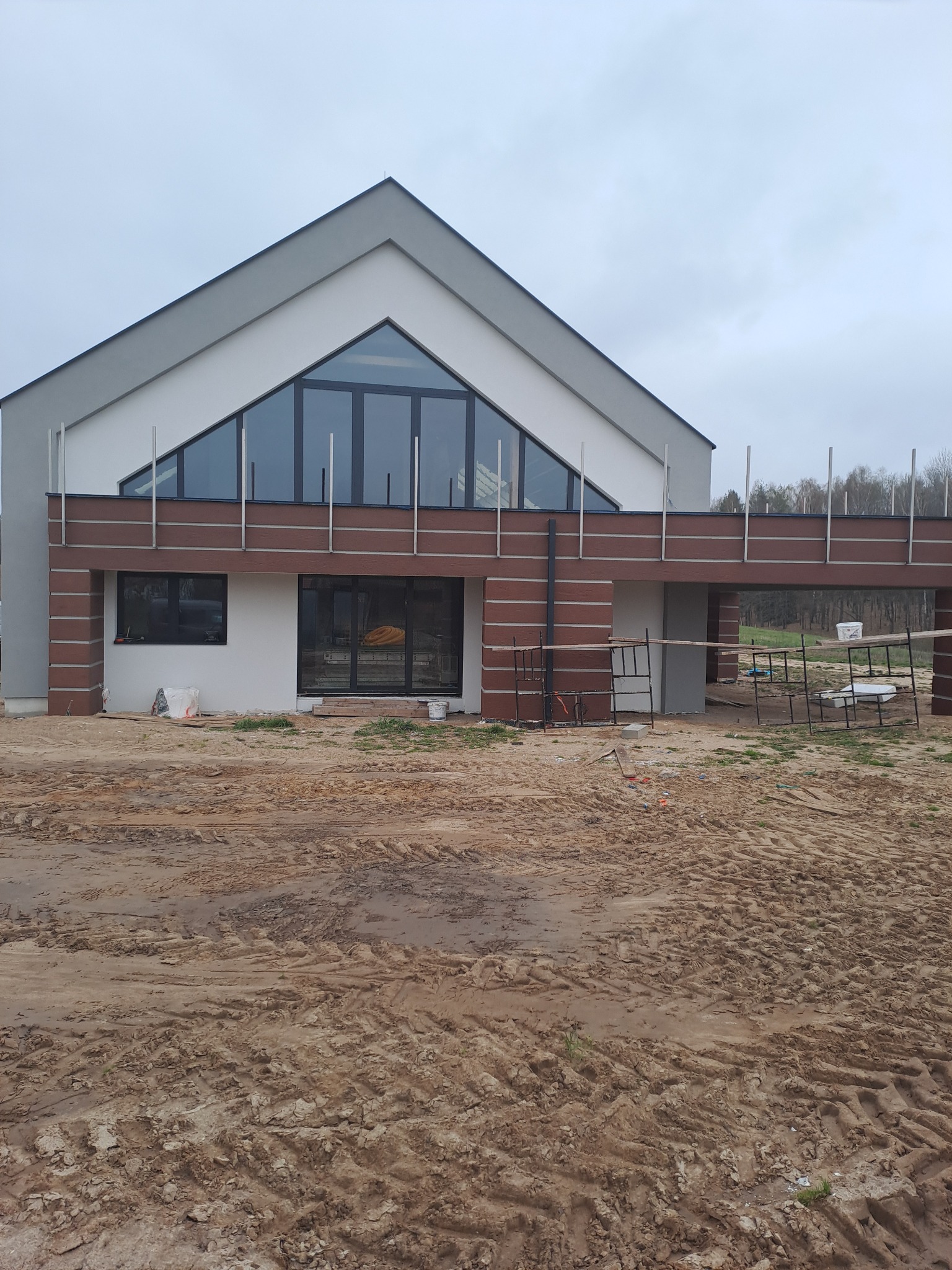 Nowoczesny dom jednorodzinny w Olsztynie w trakcie prac elewacyjnych. Widoczne rusztowania i przygotowany teren.