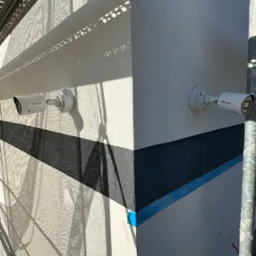 Dwie kamery monitoringu Hikvision zamontowane na świeżo pomalowanej ścianie budynku, z widocznymi śladami rusztowania i cieniem. Wykończenie elewacji w trakcie.