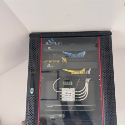 JS-Elektro - Zamknięta szafa rack z zainstalowanymi urządzeniami sieciowymi i monitoringowymi, widoczne kable Ethernet i zasilające, sprzęt marek GetFort, Hikvision i Volt.
