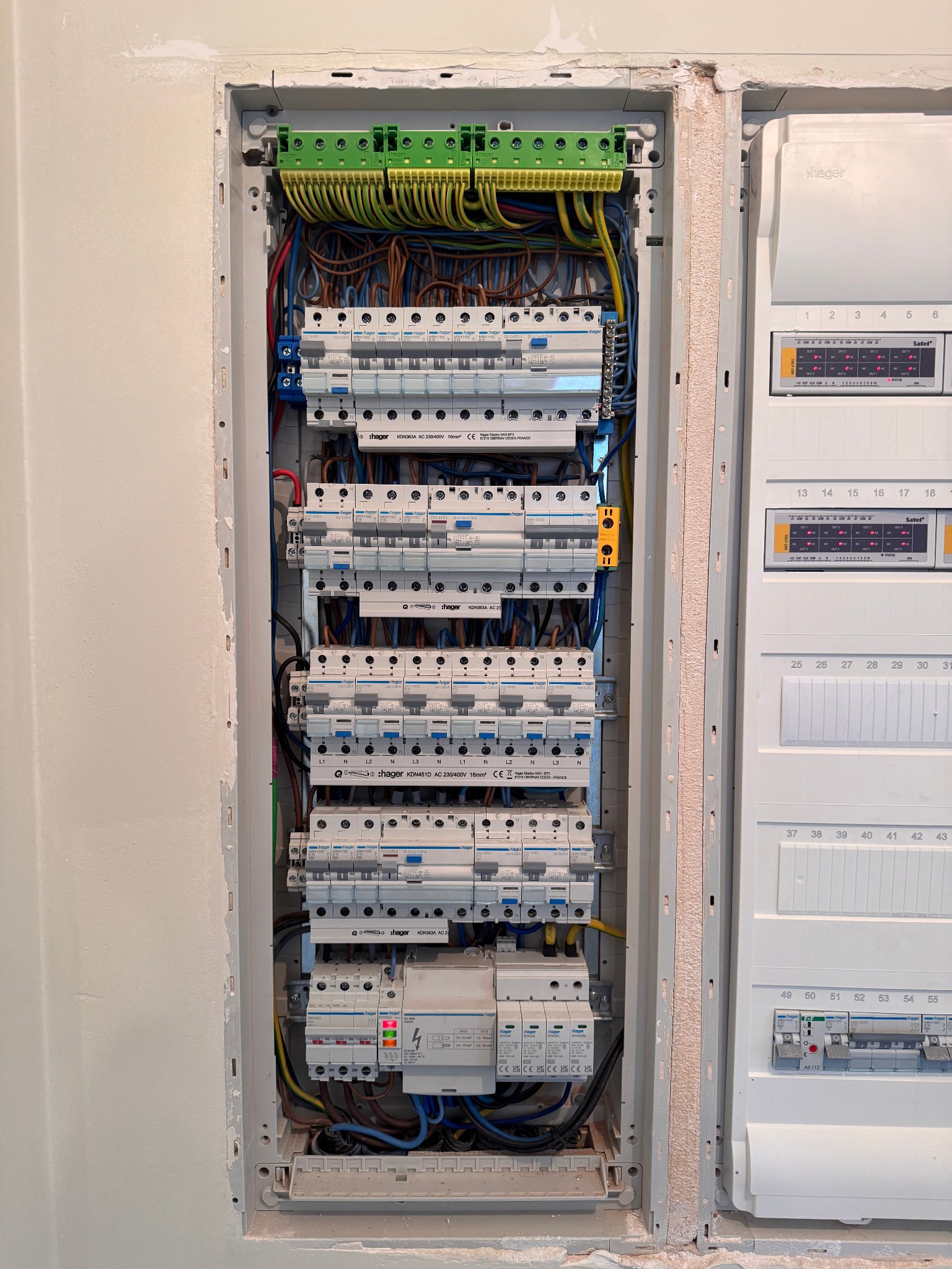Rozdzielnica elektryczna z zabezpieczeniami Hager, widoczne przewody i aparatura modułowa. Instalacja wnękowa, obok druga skrzynka z opisami obwodów.