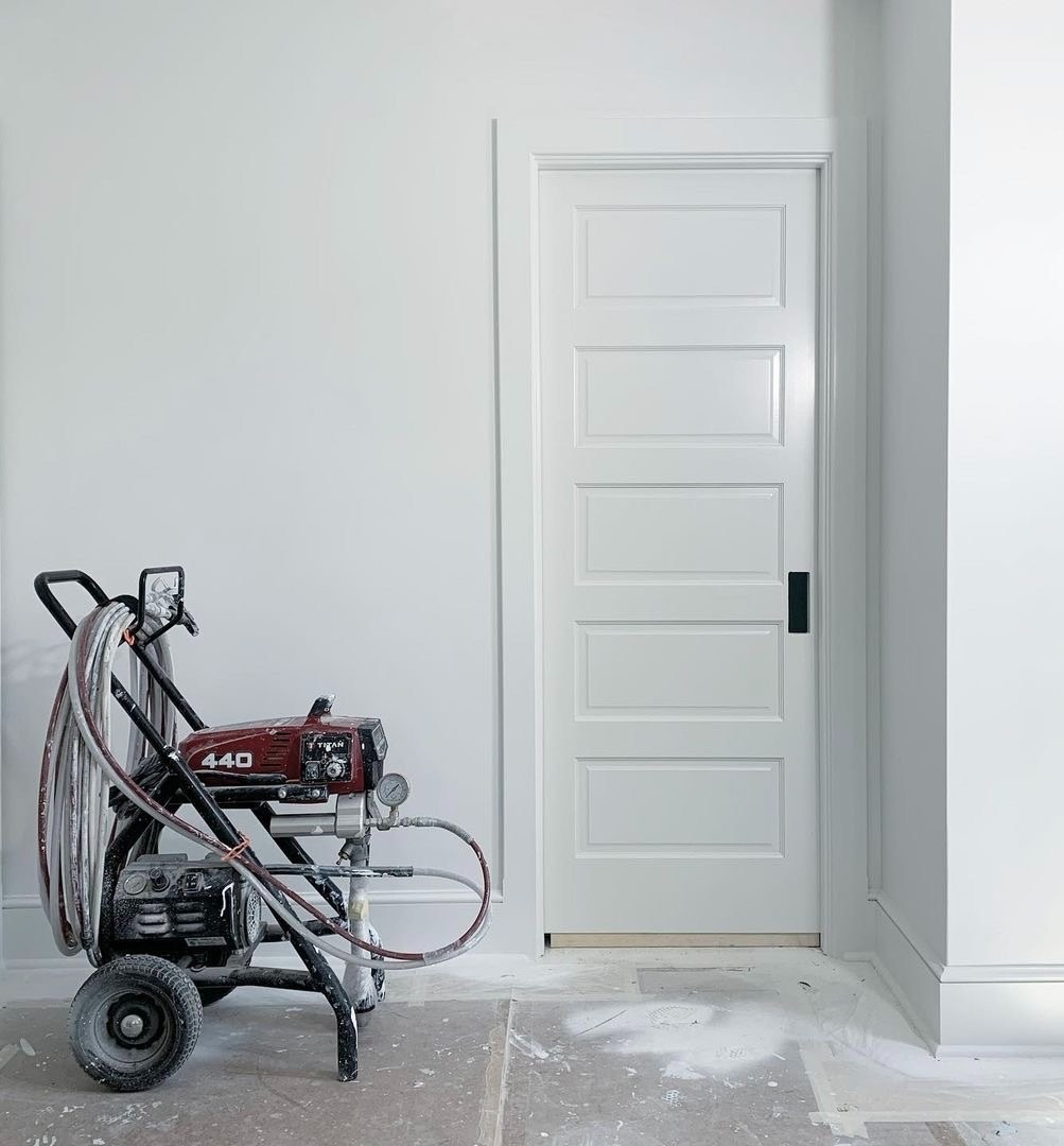 Profesjonalny agregat malarski Titan 440 na tle świeżo pomalowanej na biało ściany i drzwi z panelami, podłoga zabezpieczona folią malarską.