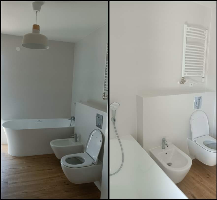 Jasna łazienka z drewnopodobną podłogą, wolnostojąca wanna, wisząca toaleta i bidet, grzejnik drabinkowy na ścianie, minimalistyczna lampa sufitowa.