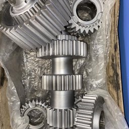 Car-Czyścik Daniel Ziaja - Metalowe koła zębate, w tym jedno z dwoma rzędami zębów na wale, po obróbce, leżące w pudełku wyłożonym folią.