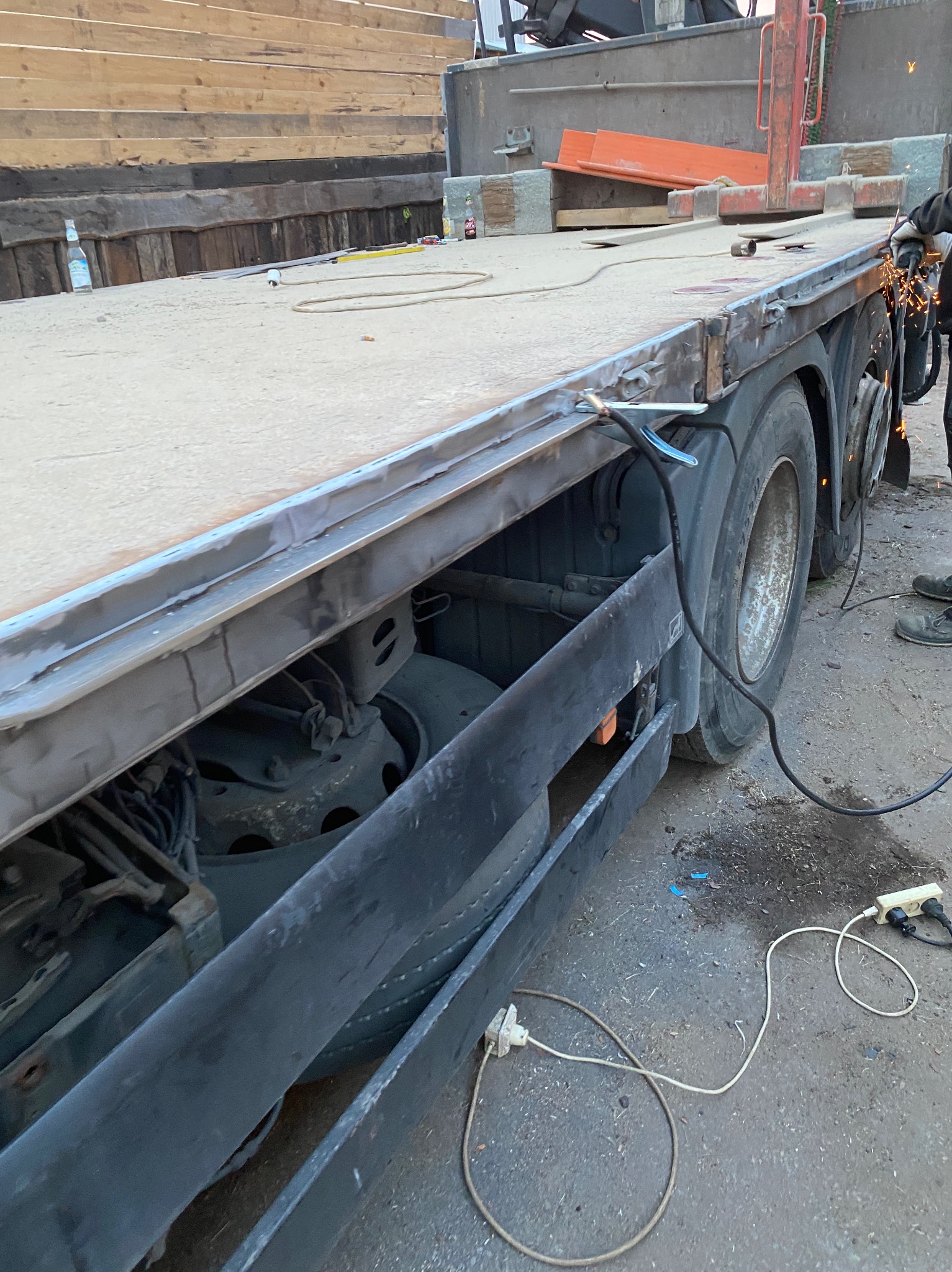 Prace spawalnicze na platformie ciężarówki, widoczne iskry, spawarka oraz częściowo sylwetka spawacza w rękawicach ochronnych.