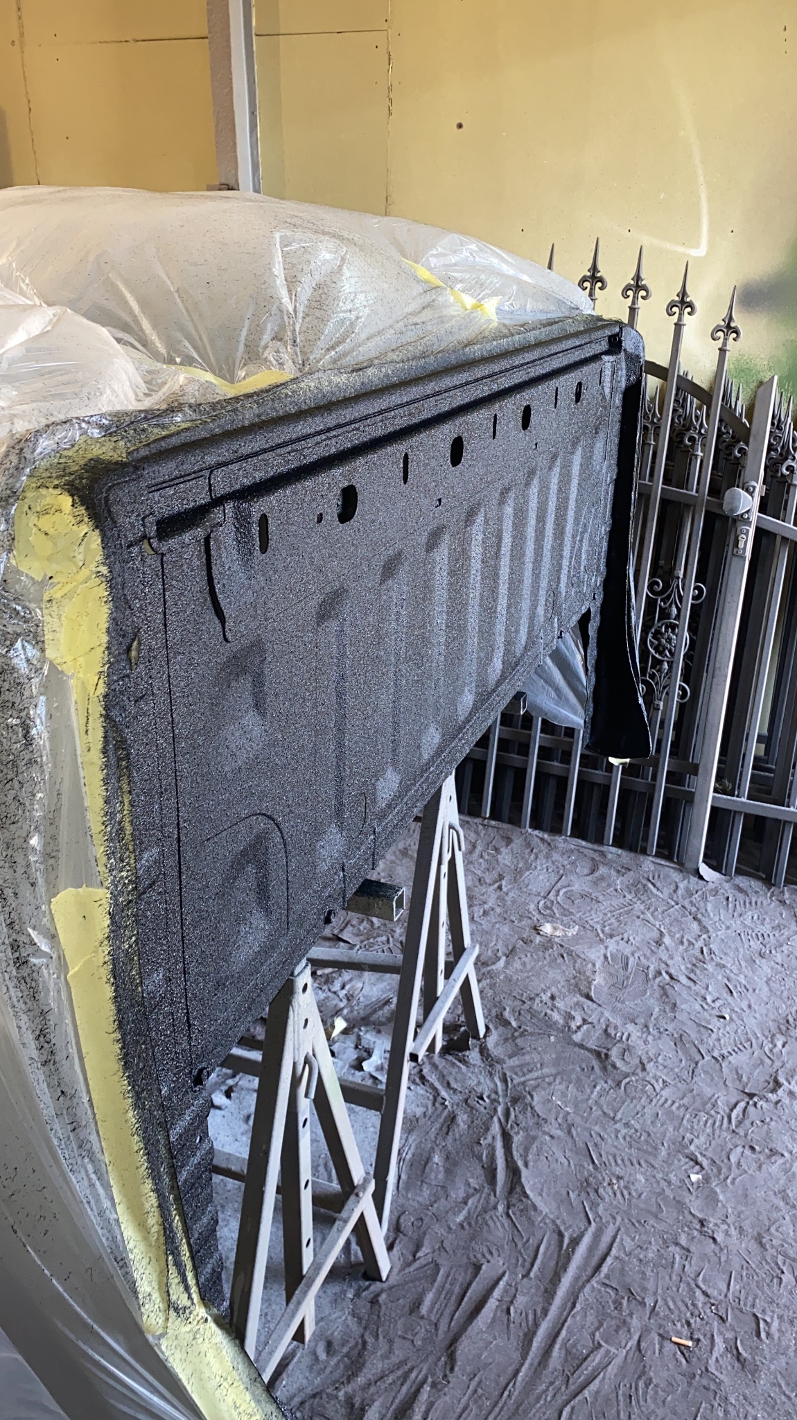 Część paki pickupa po nałożeniu ochronnej powłoki, zabezpieczona folią i taśmą, ustawiona na kozłach w warsztacie w Kolonowskim. W tle widoczne metalowe ogrodzenie.