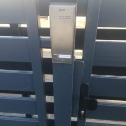 SmartConnectSystems Paweł Wierzelewski - Domofon ACO zamontowany na metalowej, poziomej bramie posesji z czarną klamką. Na domofonie widoczna naklejka z nazwiskiem 'Piotrowscy'.