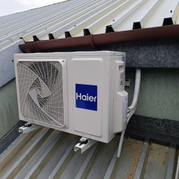 Tomasz Łabędź - Zewnętrzna jednostka klimatyzacji Haier zamontowana na metalowym dachu z widocznym brązowym orynnowaniem i fragmentami izolacji rur.