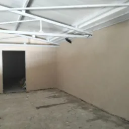 Wnętrze pomieszczenia po nałożeniu jasnobeżowych tynków. Widoczna surowa podłoga, ściany z nałożonym tynkiem oraz biała konstrukcja dachu.