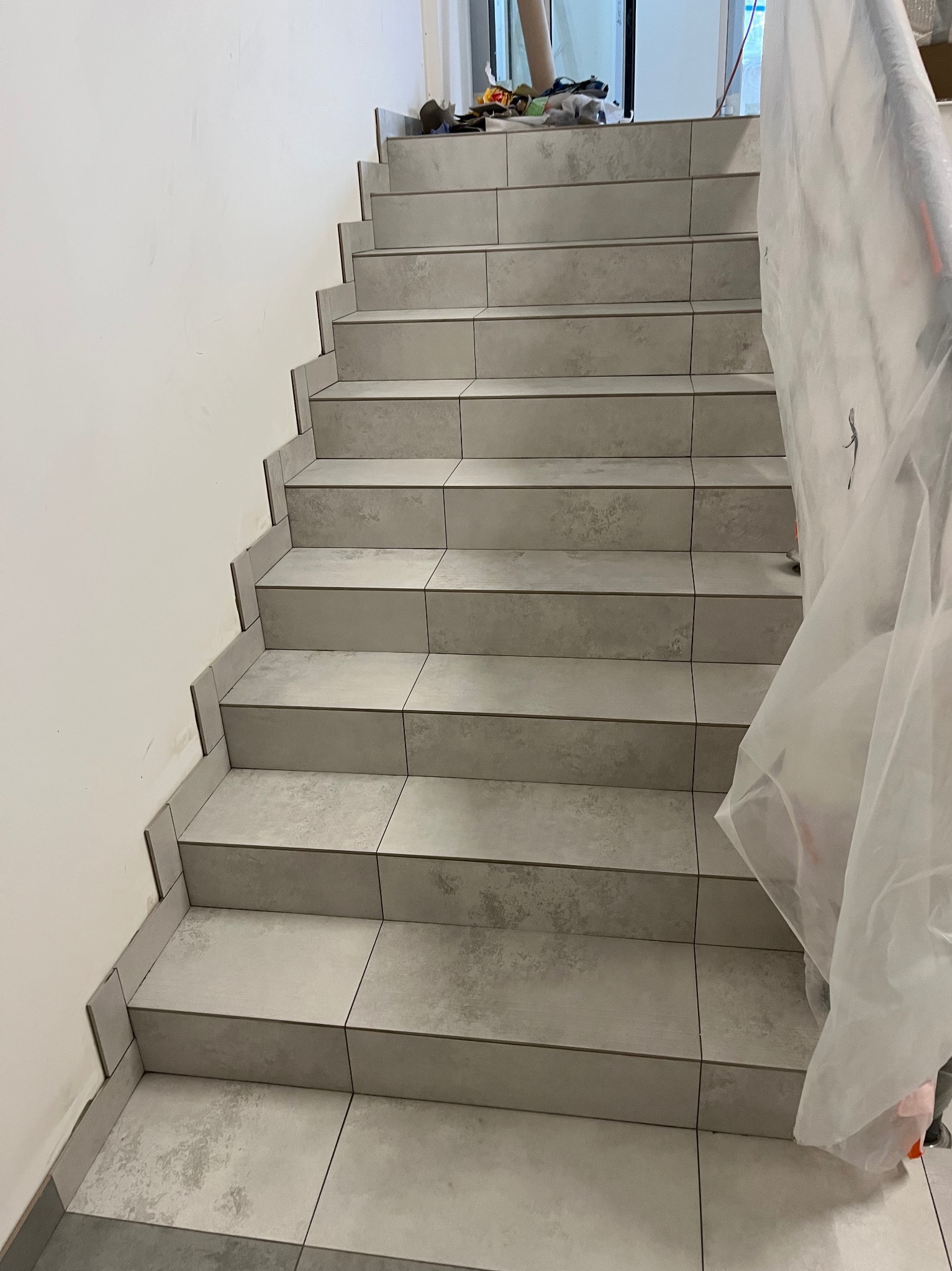 Wyłożone płytkami schody wewnątrz budynku, zabezpieczone folią malarską, widoczne narzędzia na górnym podeście.