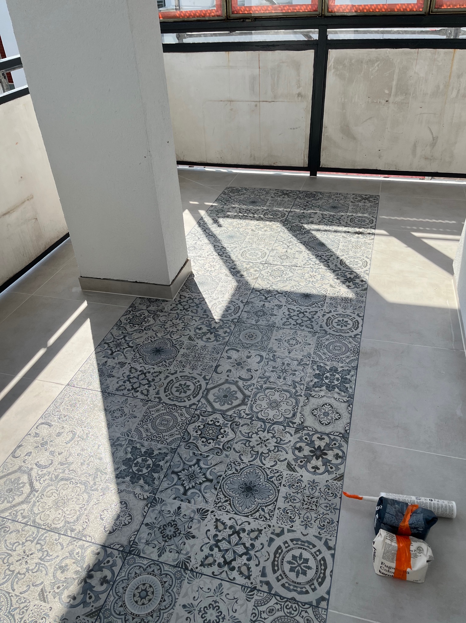 Ułożona mozaika podłogowa w odcieniach szarości na balkonie z widocznym cieniem i narzędziami do fugowania.