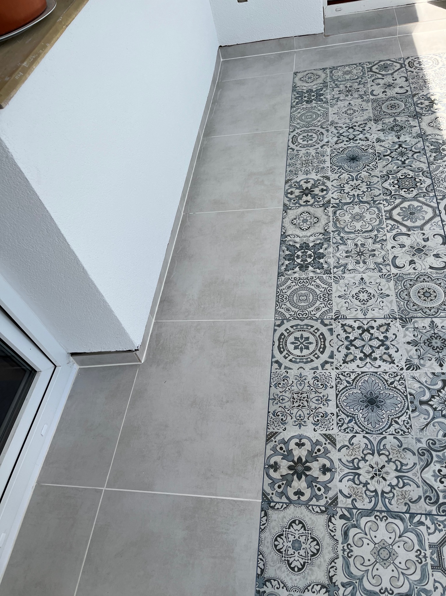 Wykończony balkon z płytkami w dwóch wzorach: szare gładkie płytki oraz płytki dekoracyjne w stylu marokańskim, ułożone pasem wzdłuż ściany.