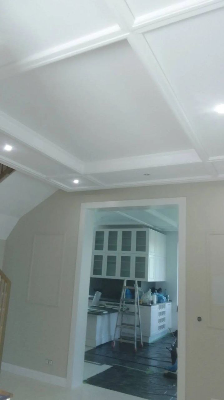 Wykończony sufit z ozdobnymi listwami i wbudowanym oświetleniem, widok na kuchnię z drabiny i zabezpieczoną podłogą.