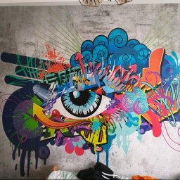 Proprofesional - Szara ściana z abstrakcyjnym, kolorowym graffiti przedstawiającym oko otoczone wzorami, strzałkami i plamami farby.