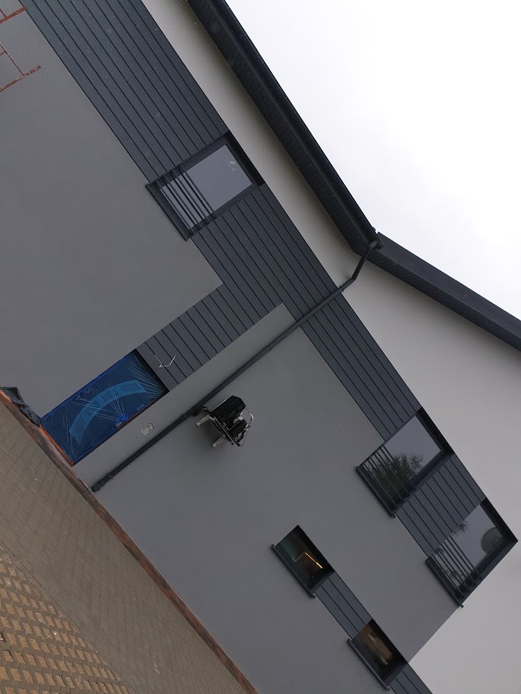 Szara elewacja domu z widocznymi oknami, zabezpieczonym oknem folią ochronną i zamontowaną lampą elewacyjną.