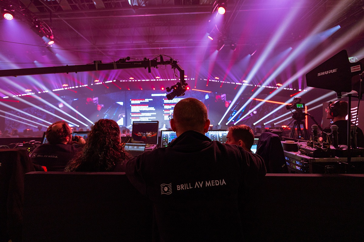 Ekipa techniczna Brill AV Media obsługuje oświetlenie i nagłośnienie podczas wydarzenia, widoczne monitory, konsolety i reflektory sceniczne.