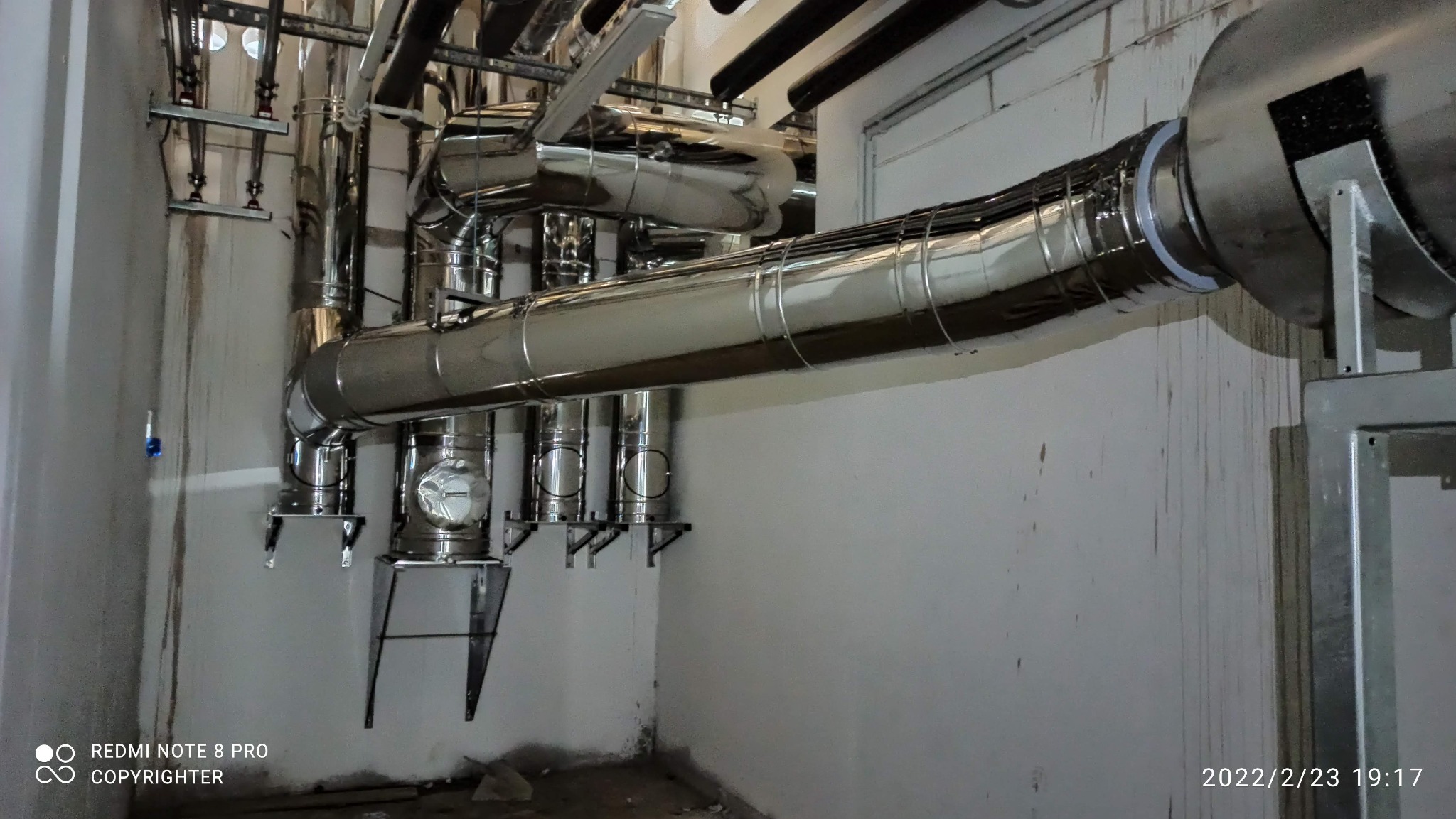 System rur wentylacyjnych ze stali nierdzewnej zamontowany przy ścianie, widoczne elementy mocujące i izolacja.