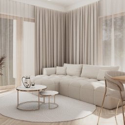 KORANTI Izabela Kornacka - Jasne wnętrze salonu z narożną sofą, okrągłym dywanem i stolikami kawowymi. Minimalistyczny design, naturalne światło, beżowa kolorystyka i tekstylne zasłony.