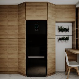 KORANTI Izabela Kornacka - Nowoczesna kuchnia z drewnianymi frontami szafek, czarną lodówką i ziołami w doniczkach, doświetlona naturalnym światłem z okna z roletami.