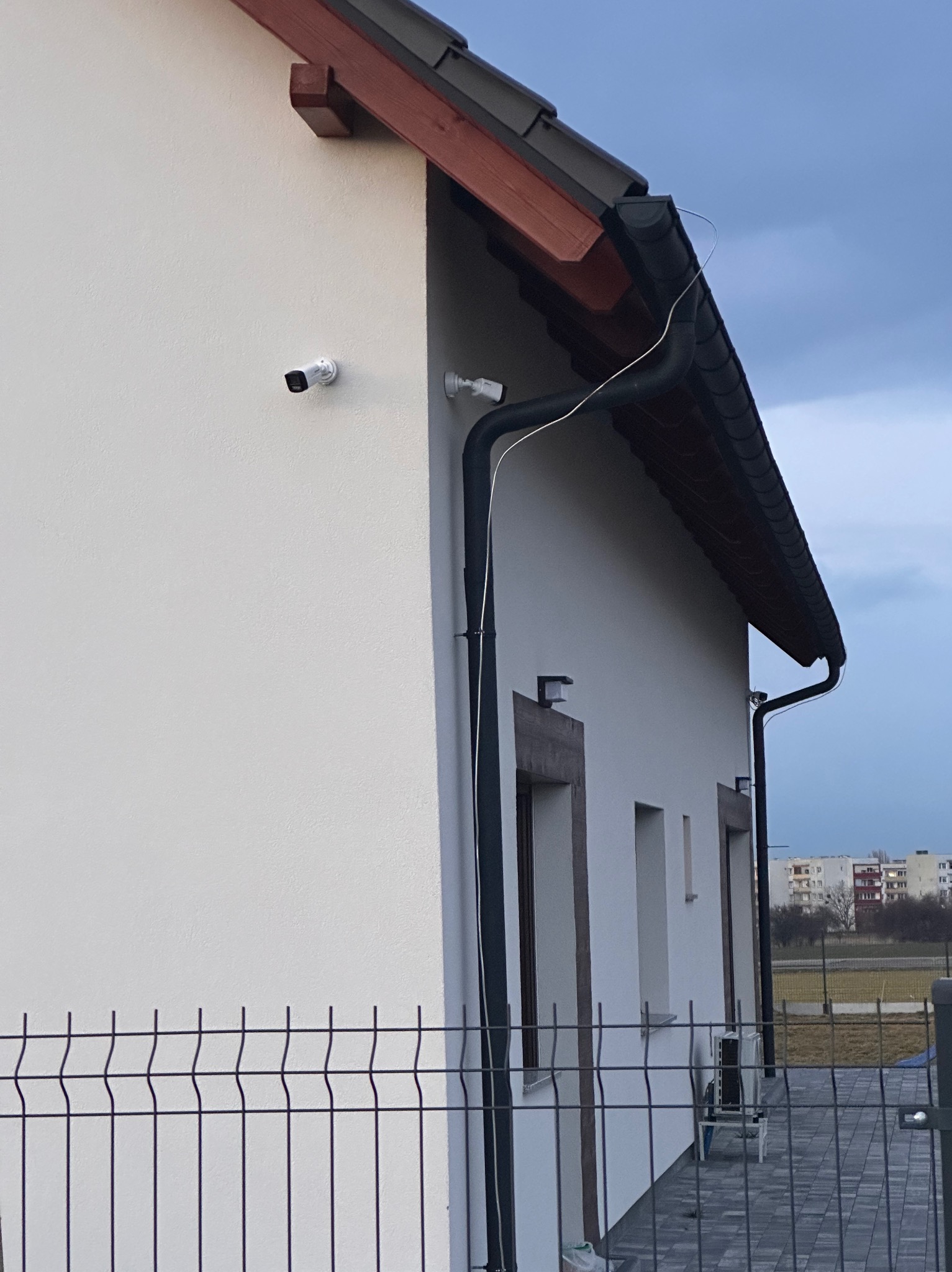 Dwie kamery monitoringu zamontowane na elewacji domu jednorodzinnego z widocznym okablowaniem biegnącym wzdłuż rynny.